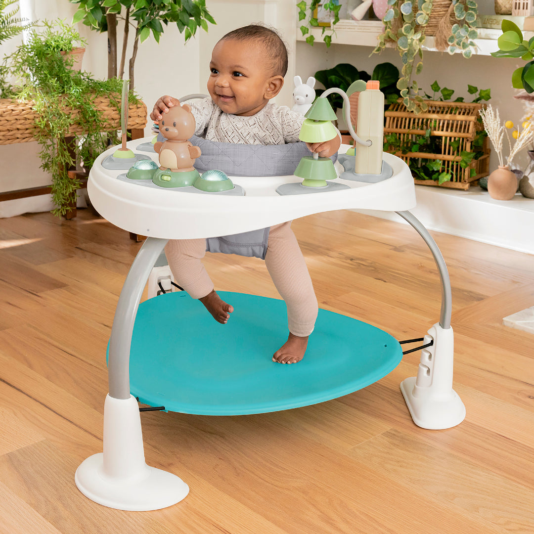 Baby in a standing and walking aid with toys on a wooden floor.