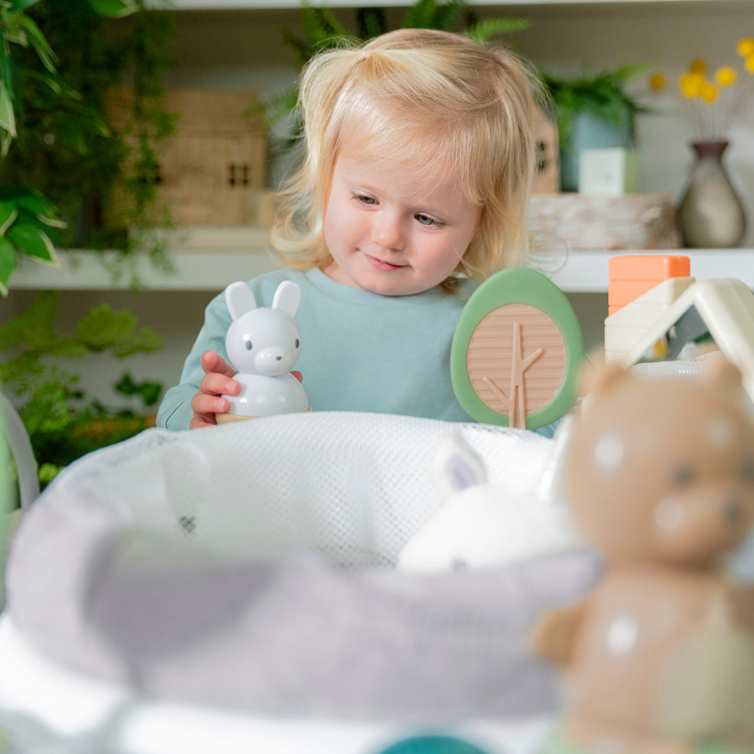 Child holding a toy rabbit in a room with plants and toys