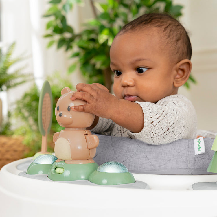 Baby interacting with a toy in a high chair with a blurred green plant background