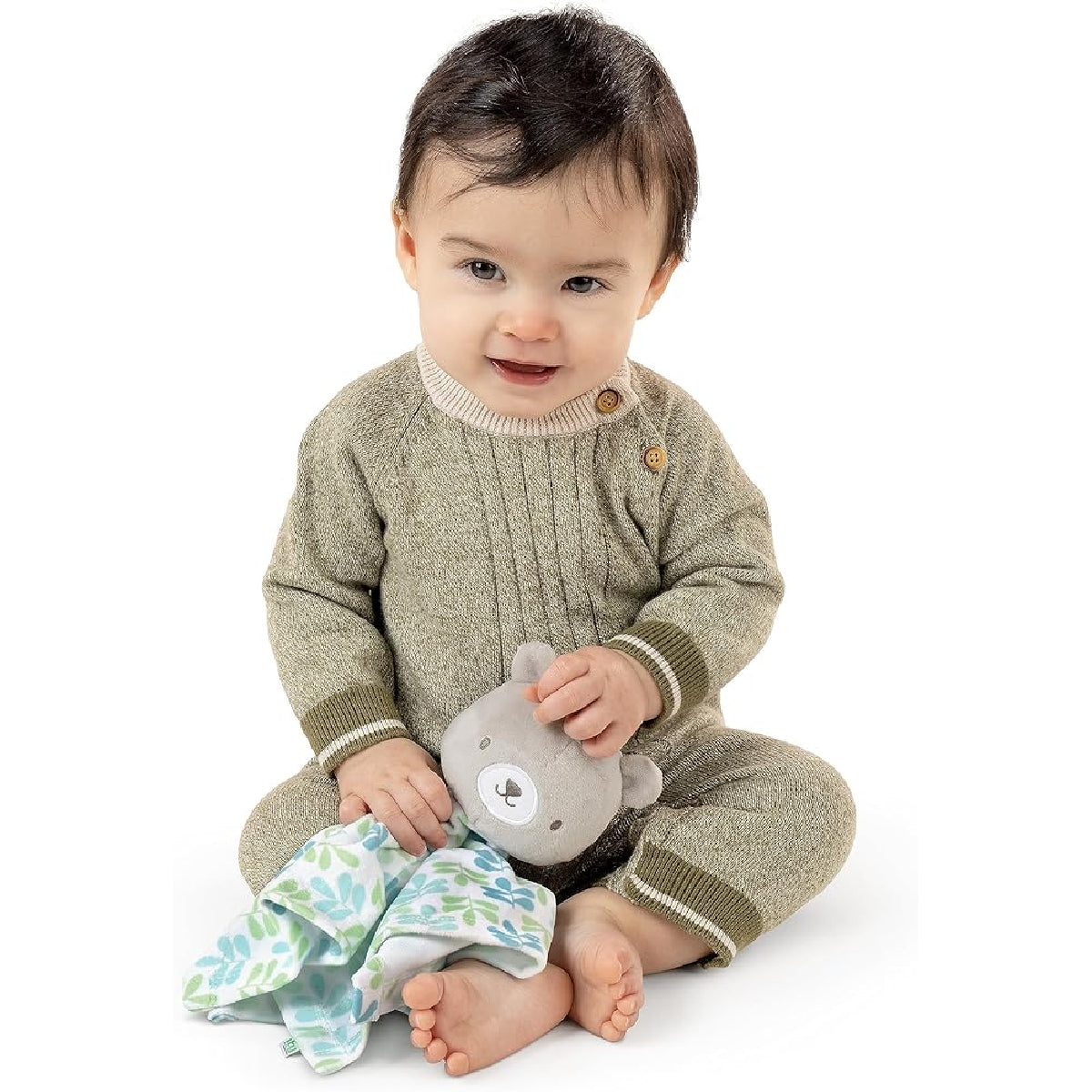 Baby wearing a green sweater and brown pants holding a gray teddy bear on a white background