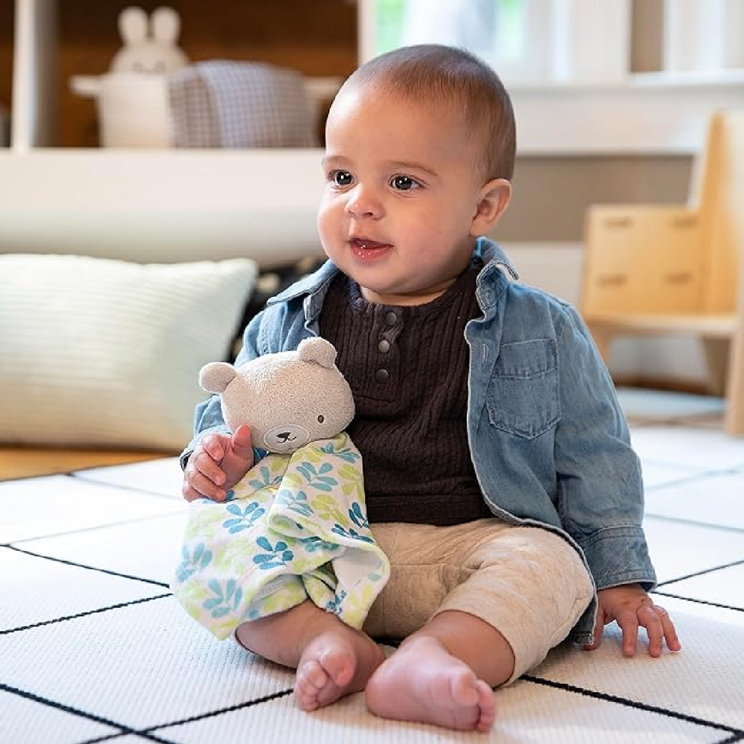 Baby sitting on a checkered floor holding a teddy bear and a cloth with a floral pattern.