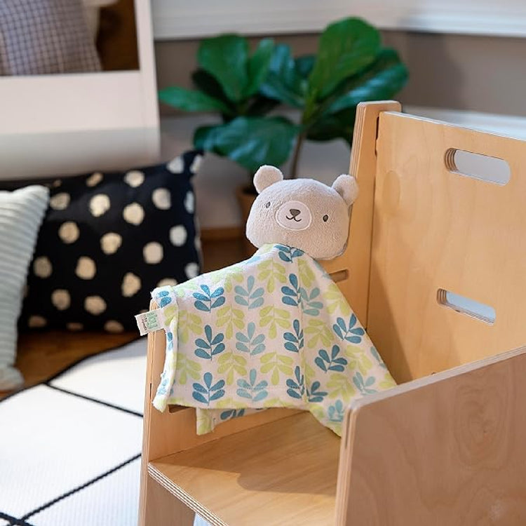 Bear-shaped toy with a floral blanket draped over a wooden shelf in a home setting.
