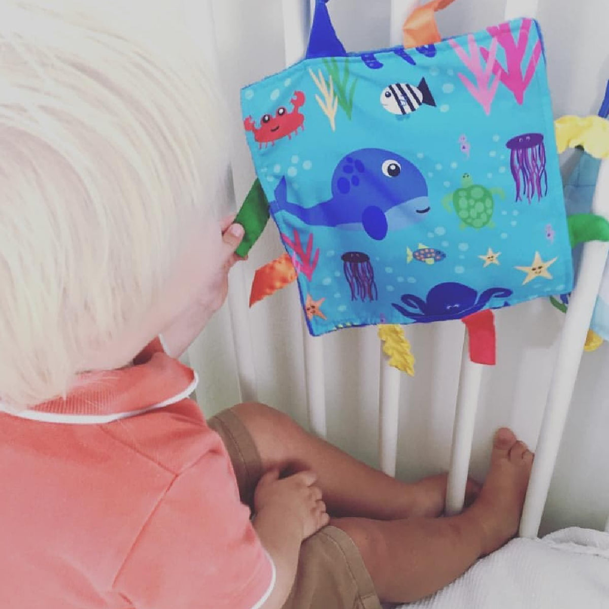 Child playing with an ocean-themed toy near a crib