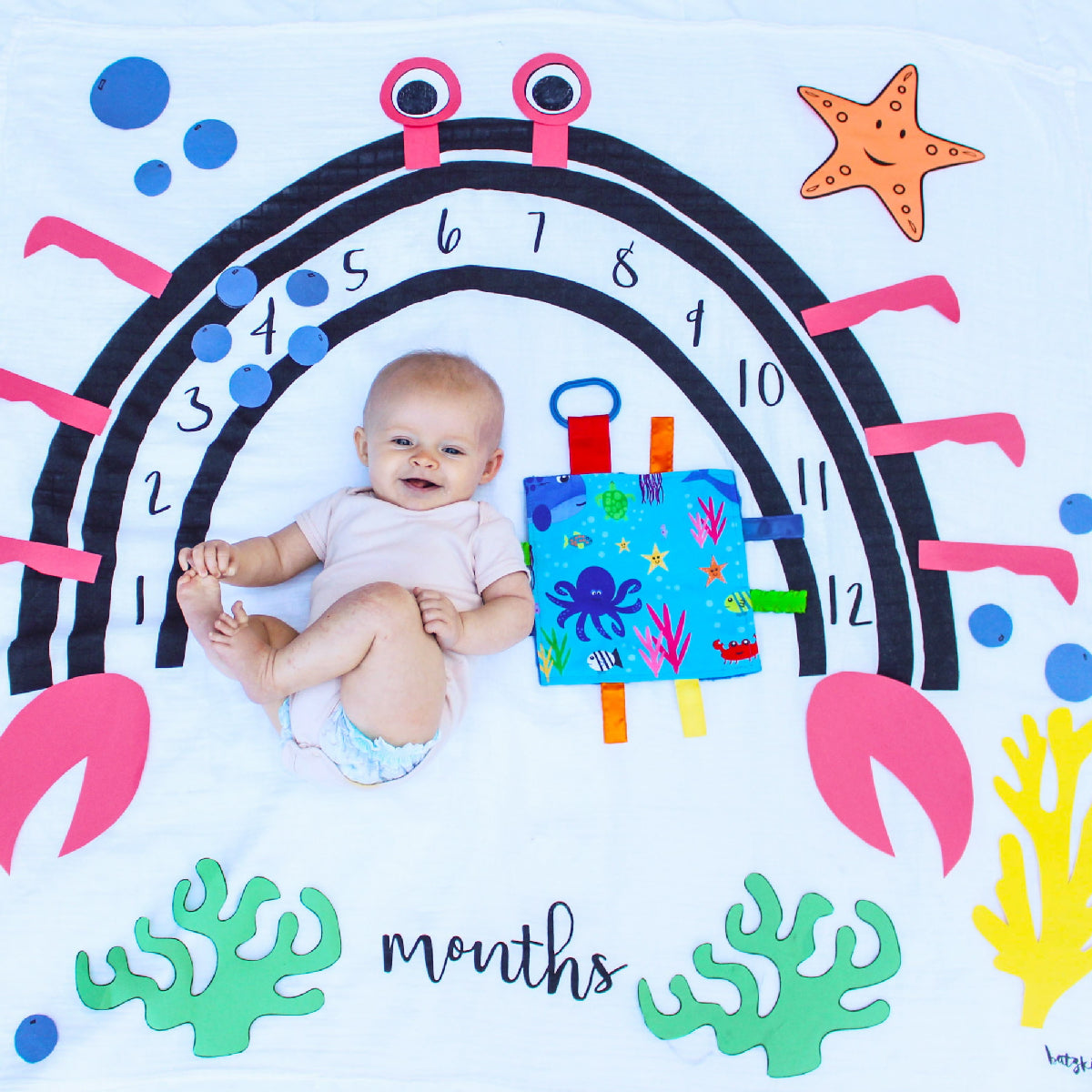 Baby lying on a milestone card with colorful sea-themed decorations and numbers.