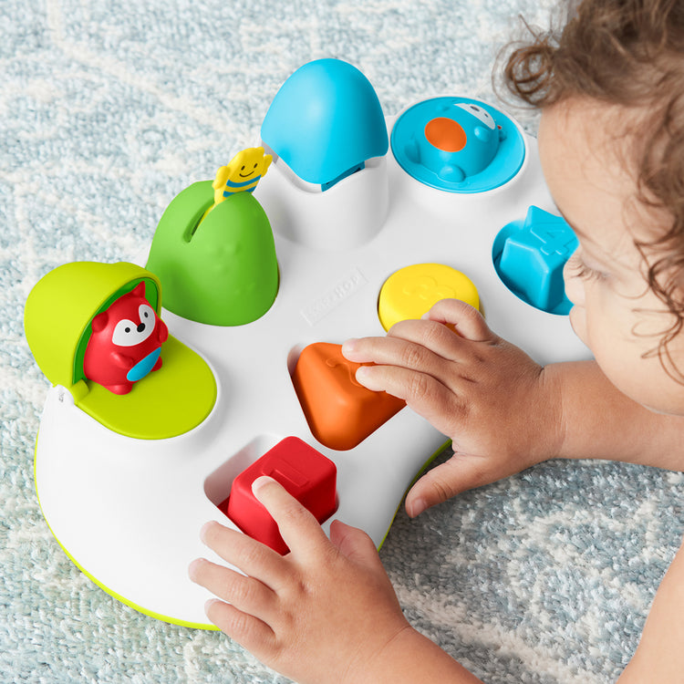 Child playing with a colorful shape sorting toy on a textured surface