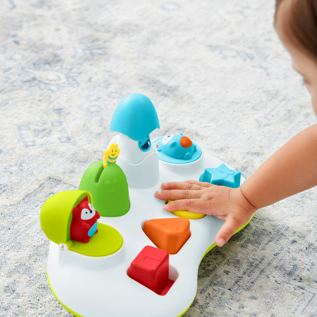 Colorful toy with geometric shapes and a child's hand interacting with it on a textured surface.