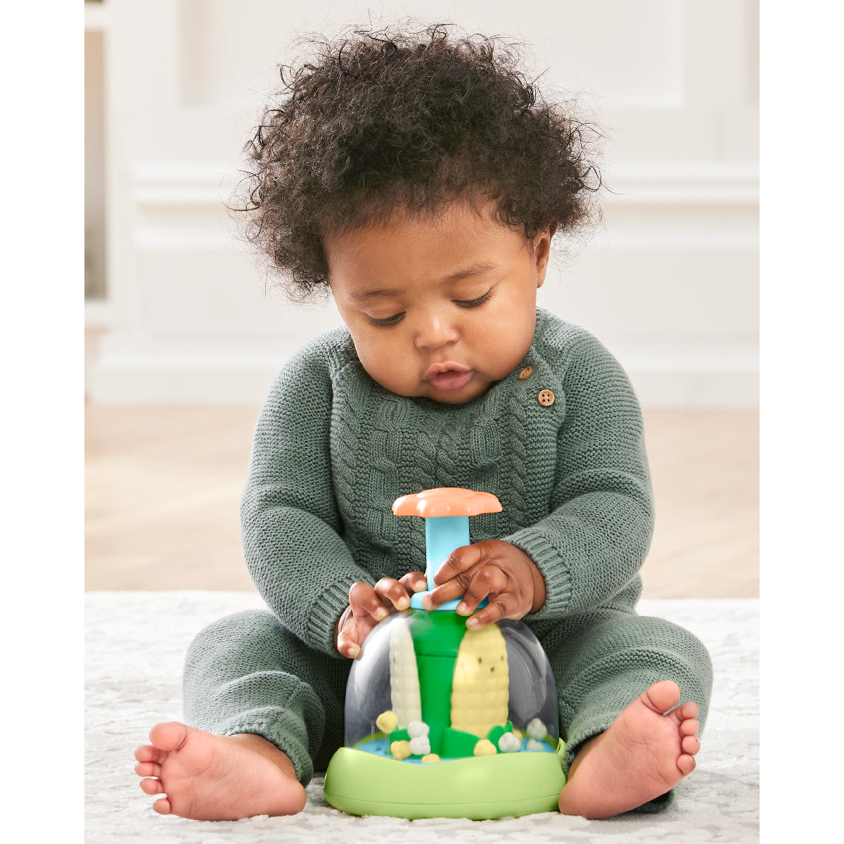 Baby playing with a green toy on a light-colored surface