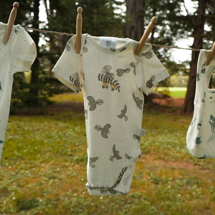 Baby rompers with bird pattern hanging on a clothesline outdoors.