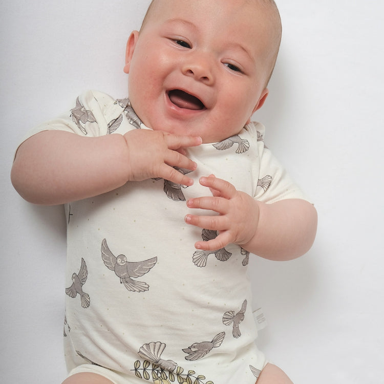 Baby wearing a white onesie with gray bird patterns on a plain background