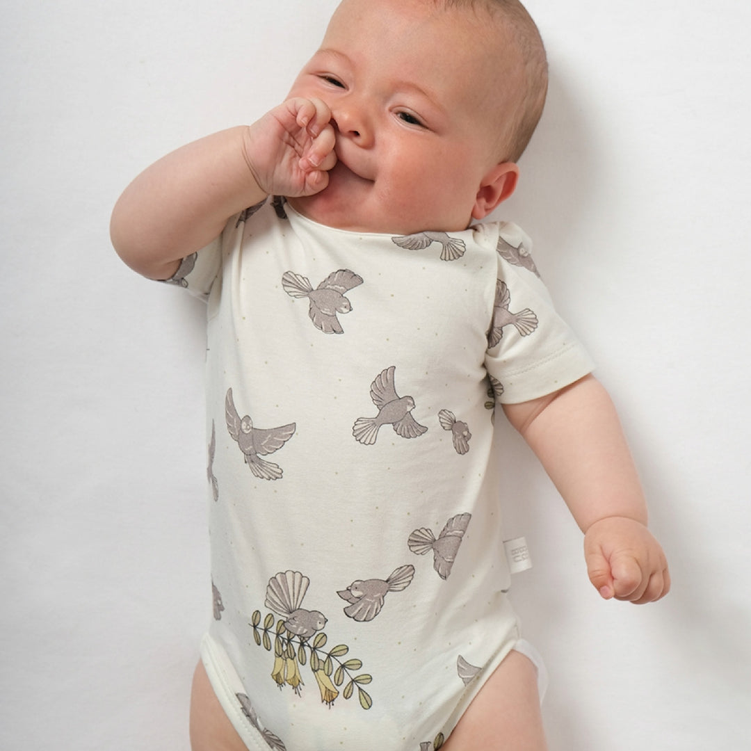 Baby wearing a white onesie with gray bird patterns on a plain background