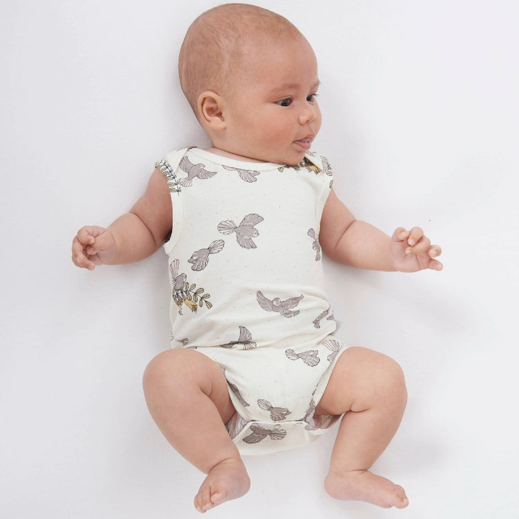 Baby wearing a white sleeveless romper with gray floral patterns on a light gray background