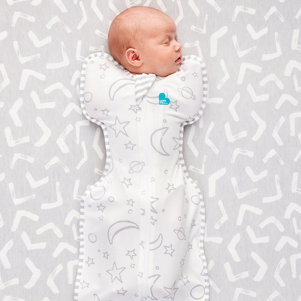 Baby wrapped in a white swaddle with star and moon patterns on a light gray background