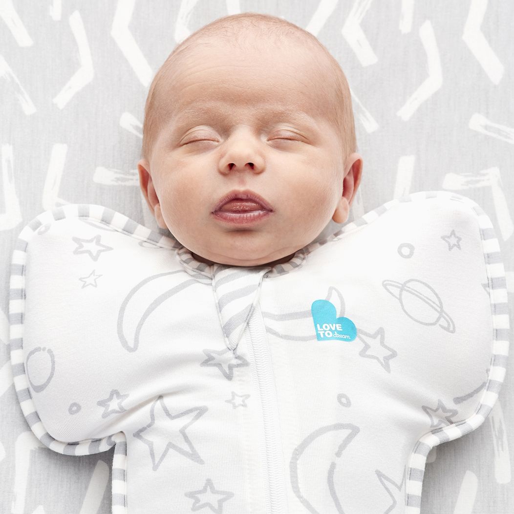 Newborn baby sleeping in a white swaddle with star and moon patterns, featuring the 'Love to Dream' brand.