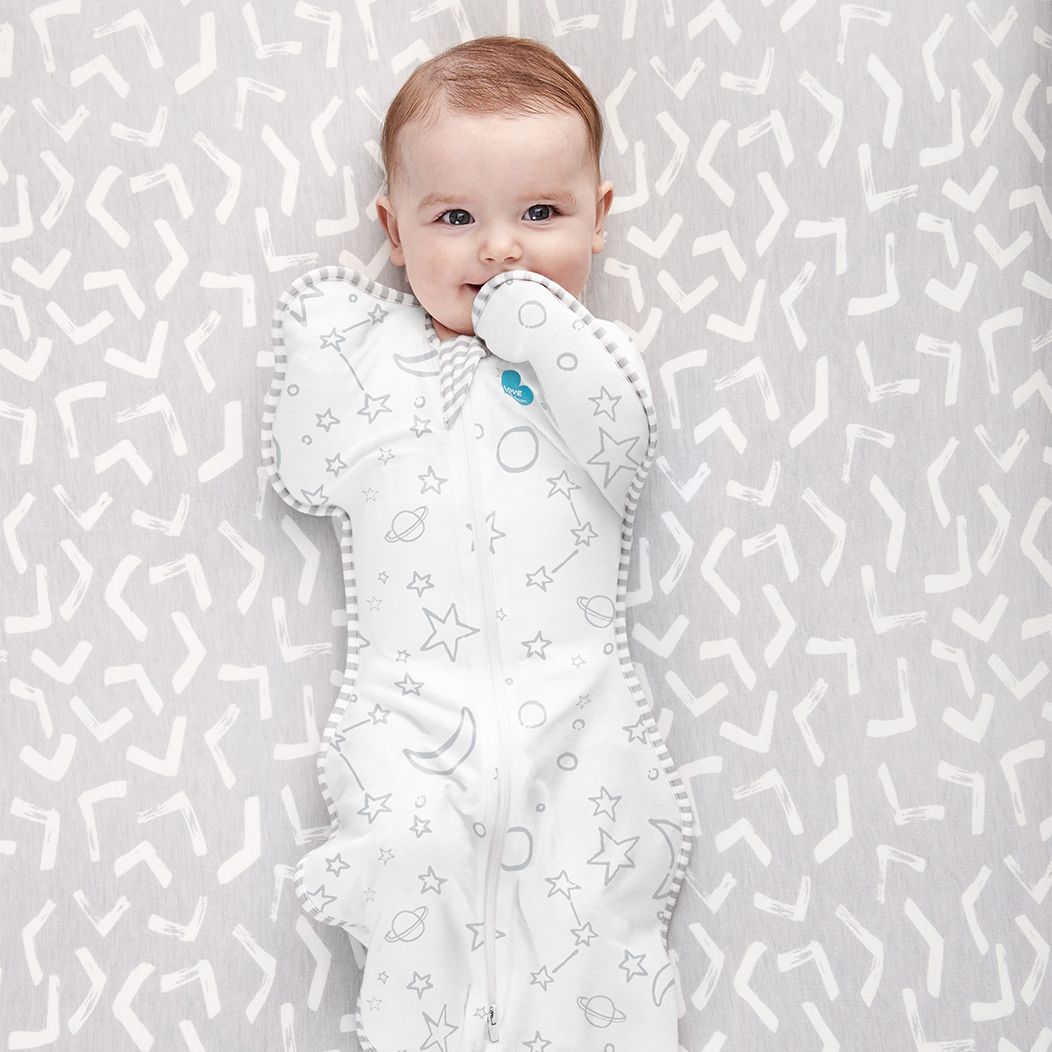 Baby lying on a patterned surface wearing a white baby comfort blanket with star and moon designs.