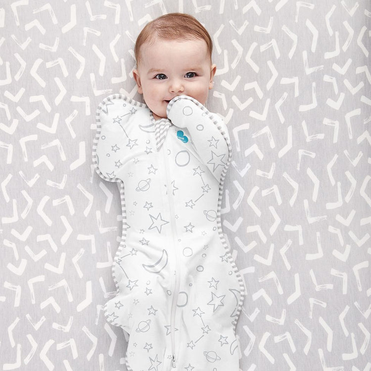 Baby lying on a patterned surface wearing a white baby comfort blanket with star and moon designs.